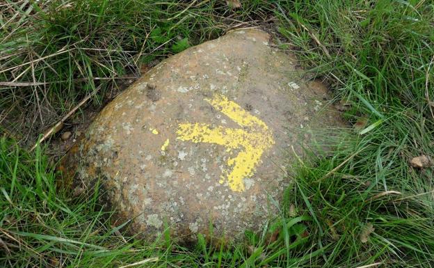 Imagen de una piedra pintada con la flecha amarilla que indica el trazado del Camino de Santiago.