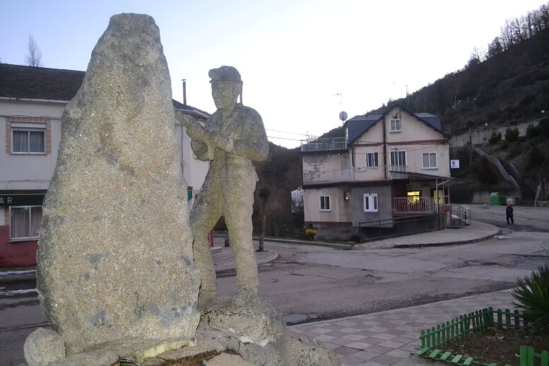 La estatua de un minero en la plaza del pueblo y, al fondo, el único bar que permanece abierto en Tremor de Arriba. 