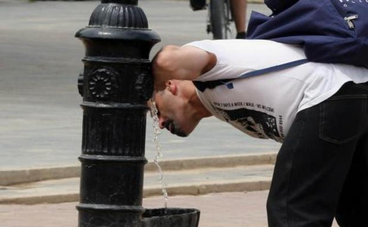 Un joven se refresca en un caño.