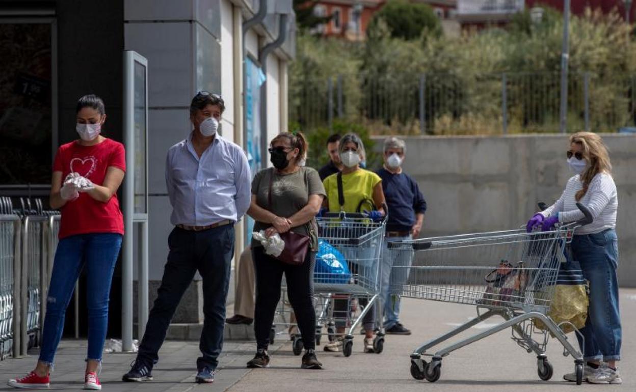 Varias personas protegidas con mascarillas hacen cola hoy en la entrada de un supermercado 