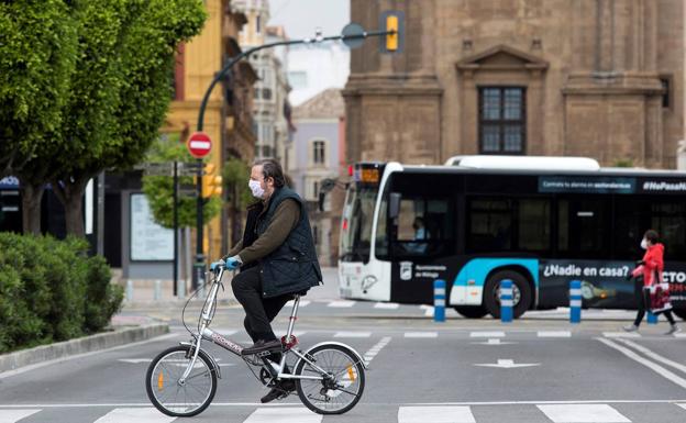 Un hombre circula en bicicleta por las calles de Málaga protegido con mascarilla y guantes.
