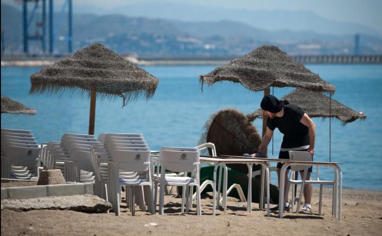 Un camarero limpia las mesas de una terraza en la playa de Málaga.