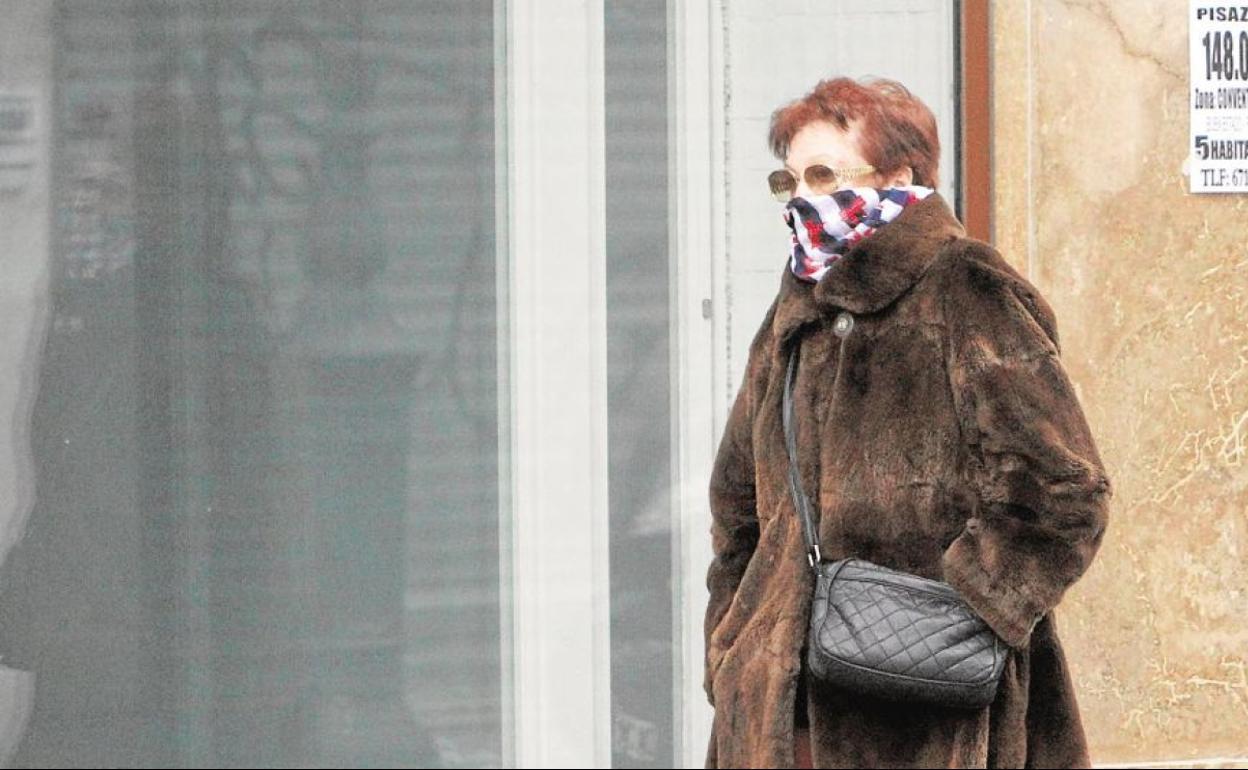 Una mujer pasea con un abrigo por la calle.