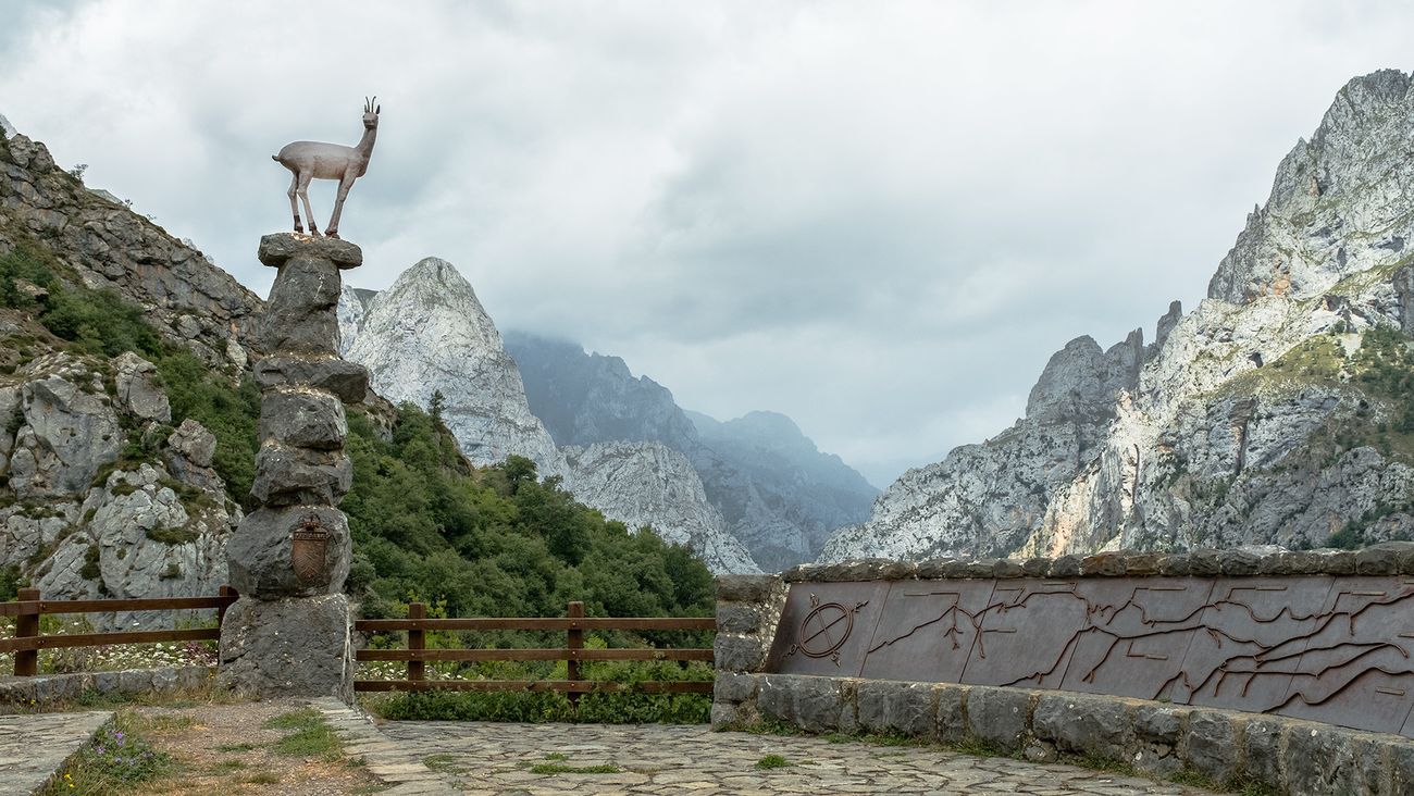 Mirador del Tombo | El mirador del Tombo, se encuentra situado en un lugar privilegiado de los Picos de Europa. Se ubica en la carretera que une Posada de Valdeón con el pequeño pueblo de Caín, poco después de atravesar Cordiñanes de Valdeón en dirección a Caín, a 50 metros del río Cares. Fue inaugurado el 10 de agosto de 1964 por el entonces ministro de información y turismo Manuel Fraga Iribarne. En el lugar se erige una cruz de hierro y una columna de piedra sobre la que se sitúa la escultura de un rebeco, obra de José Luis Coomonte. Cuenta con un grabado en el que se enumeran todas las cimas que pueden distinguirse desde el lugar, con su perfil, para facilitar la identificación. Una de ellas es el Monte Corona, lugar donde según la tradición don Pelayo fue nombrado jefe de los cristianos en el inicio de la reconquista en España.