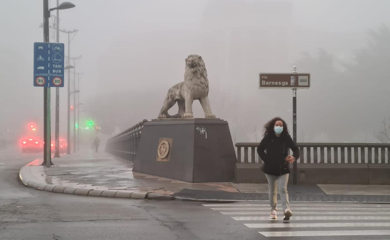 Una mujer cruza un paso de peatones en el Puente de los Leones, entre la niebla. 