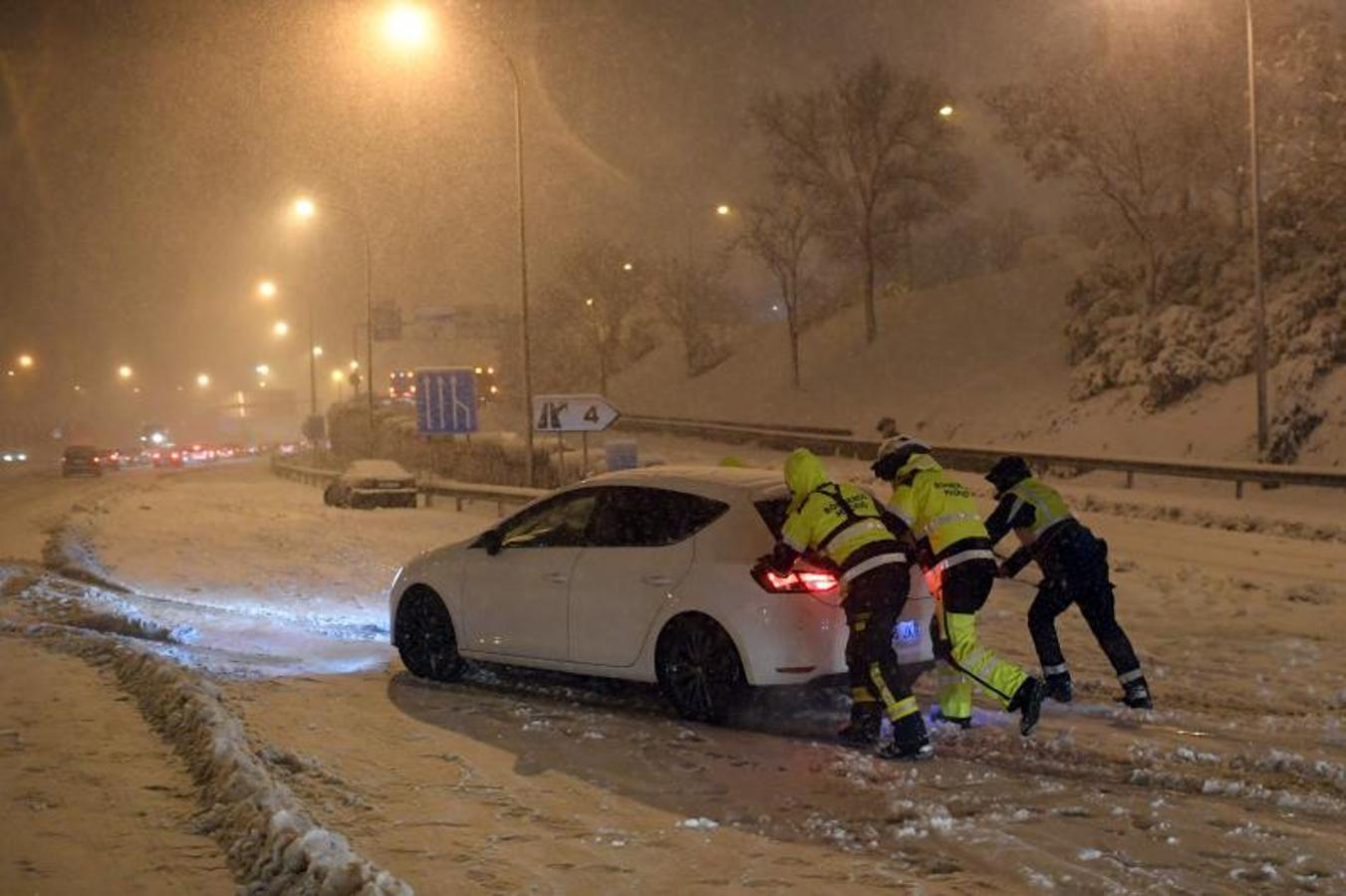 Los bomberos empujan un vehículo atascado en la carretera de circunvalación M30 en Madrid.