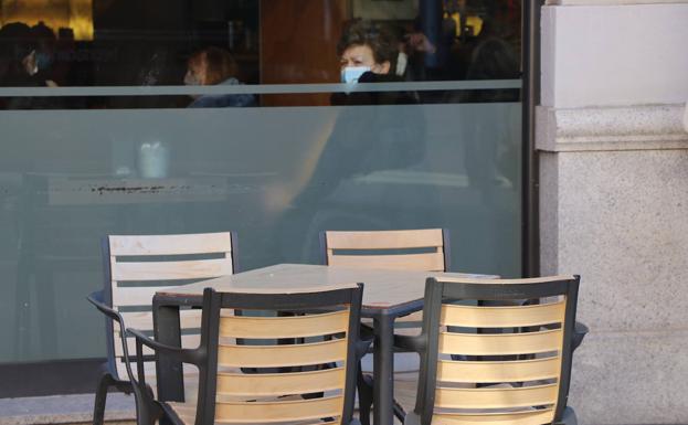 Galería. Una señora observa el exterior mientras se toma un café con la terraza vacía.