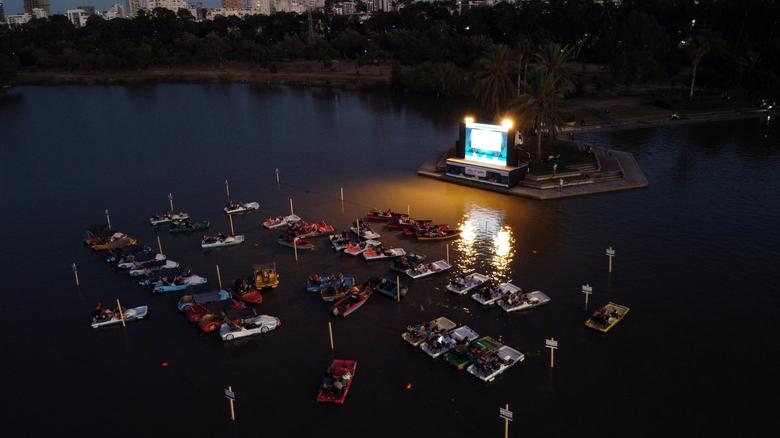 Personas se sientan en botes y ven la proyección de una película durante una vista previa para los miembros de los medios de comunicación del cine flotante "sail-in" del municipio de Tel Aviv, en el lago con botes del parque HaYarkon en Tel Aviv, Israel