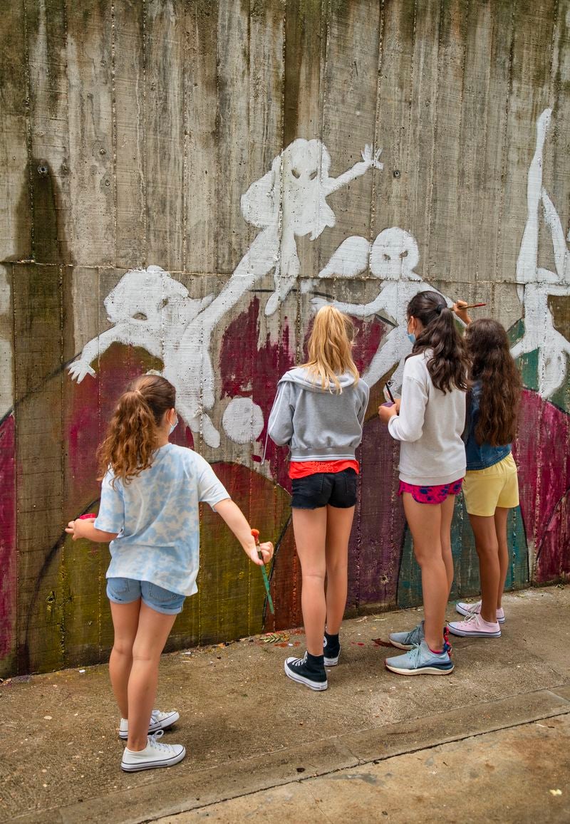 Un mural de superheroínas visibilizará el deporte femenino en el CEIP Margarita Salas de Arroyo (Valladolid), centro vencedor del reto de Afedecyl, impulsado por Iberdrola. En la imagen las niñas que están pintando el mural, junto a los responsables de la iniciativa y profesoras del centro; entre ellos, el dibujante leonés 'lolo'. 