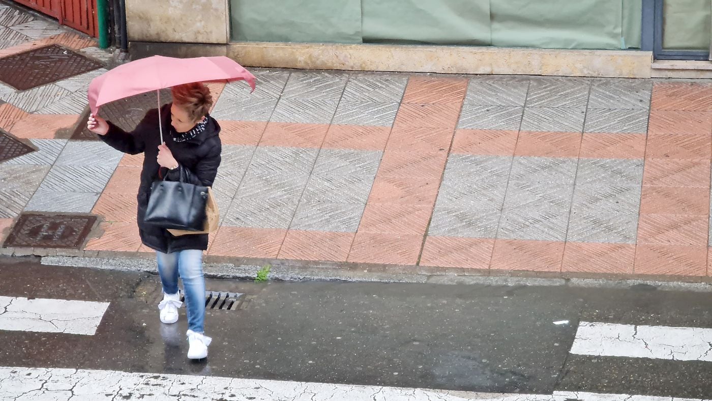 Una mujer cruza un paso de peatones en la tarde de este lunes en León capital al mismo tiempo que evita la lluvia. 