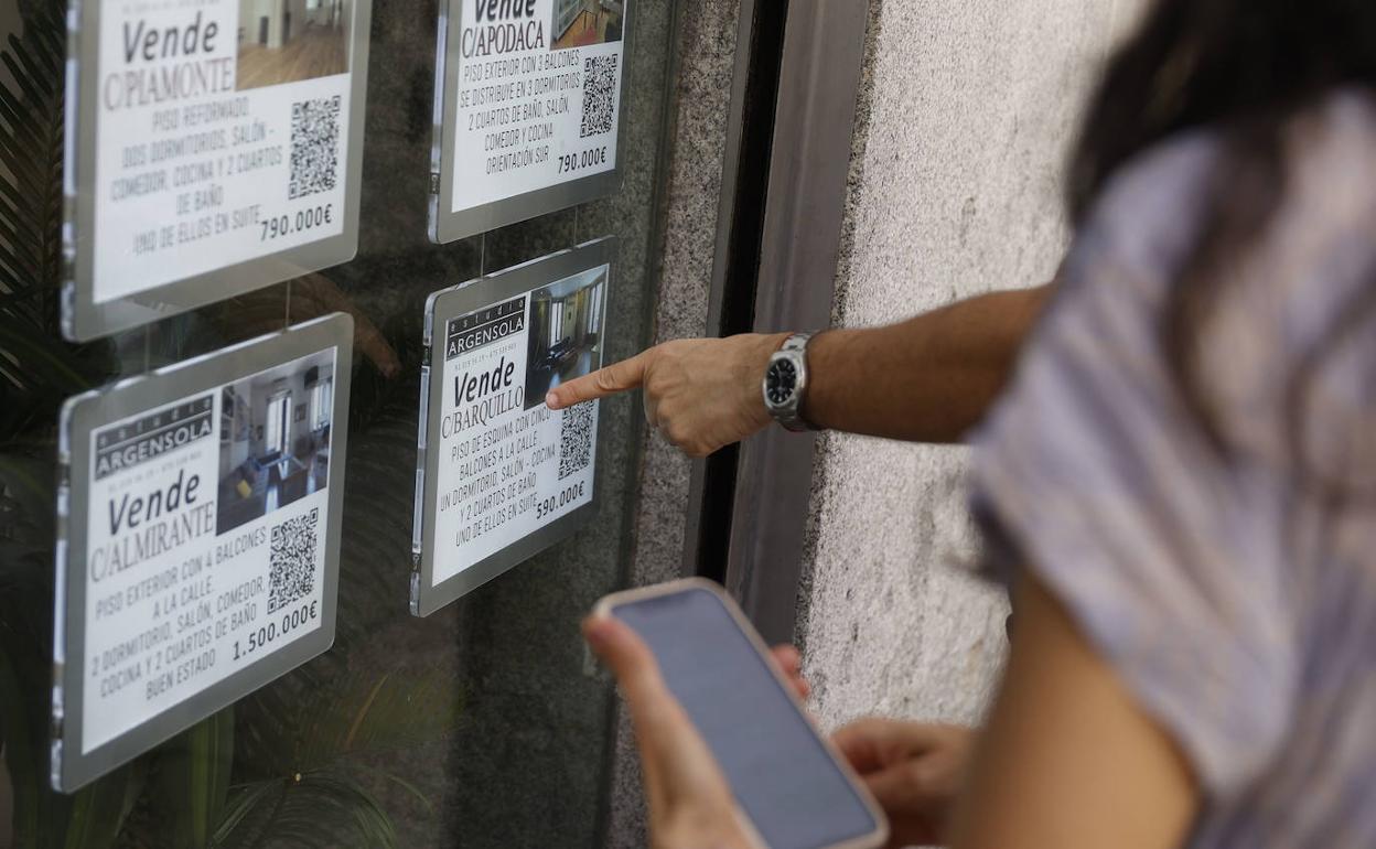 Unas personas miran el escaparate de una inmobiliaria. 