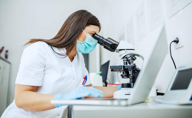 Una investigadora mira por el microscopio.