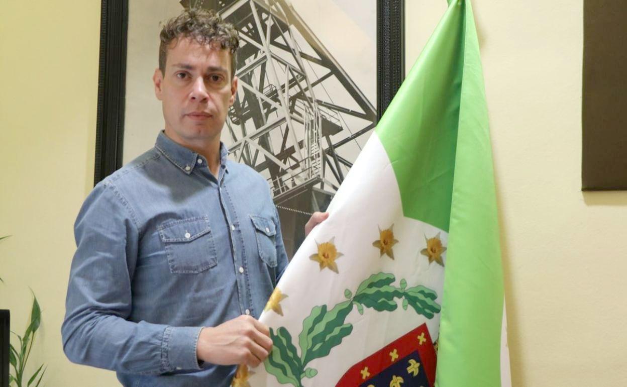 El alcalde de la localidad, Mario Rivas, posa junto a la bandera de la comarca. 