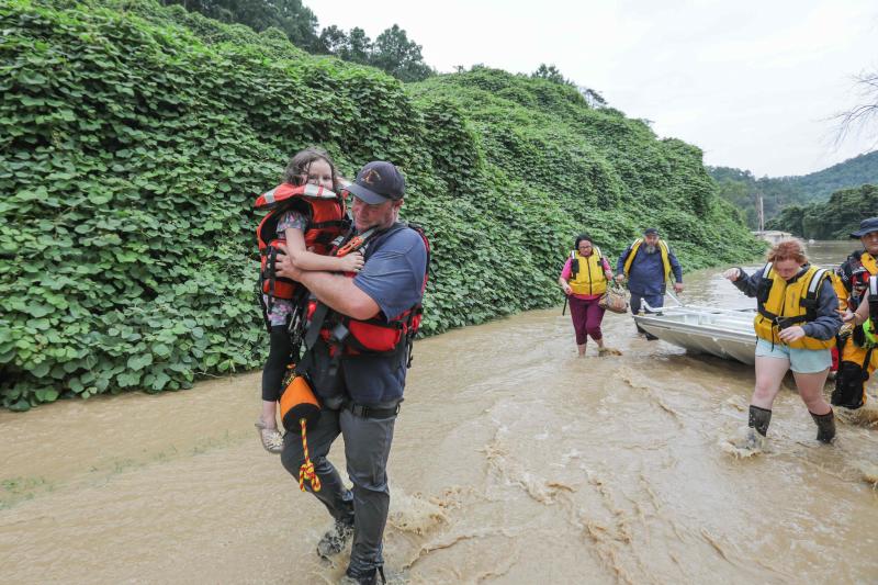 Un rescatista lleva en brazos a una niña tras evacuar a su familia debido a la crecida del río Jackson 