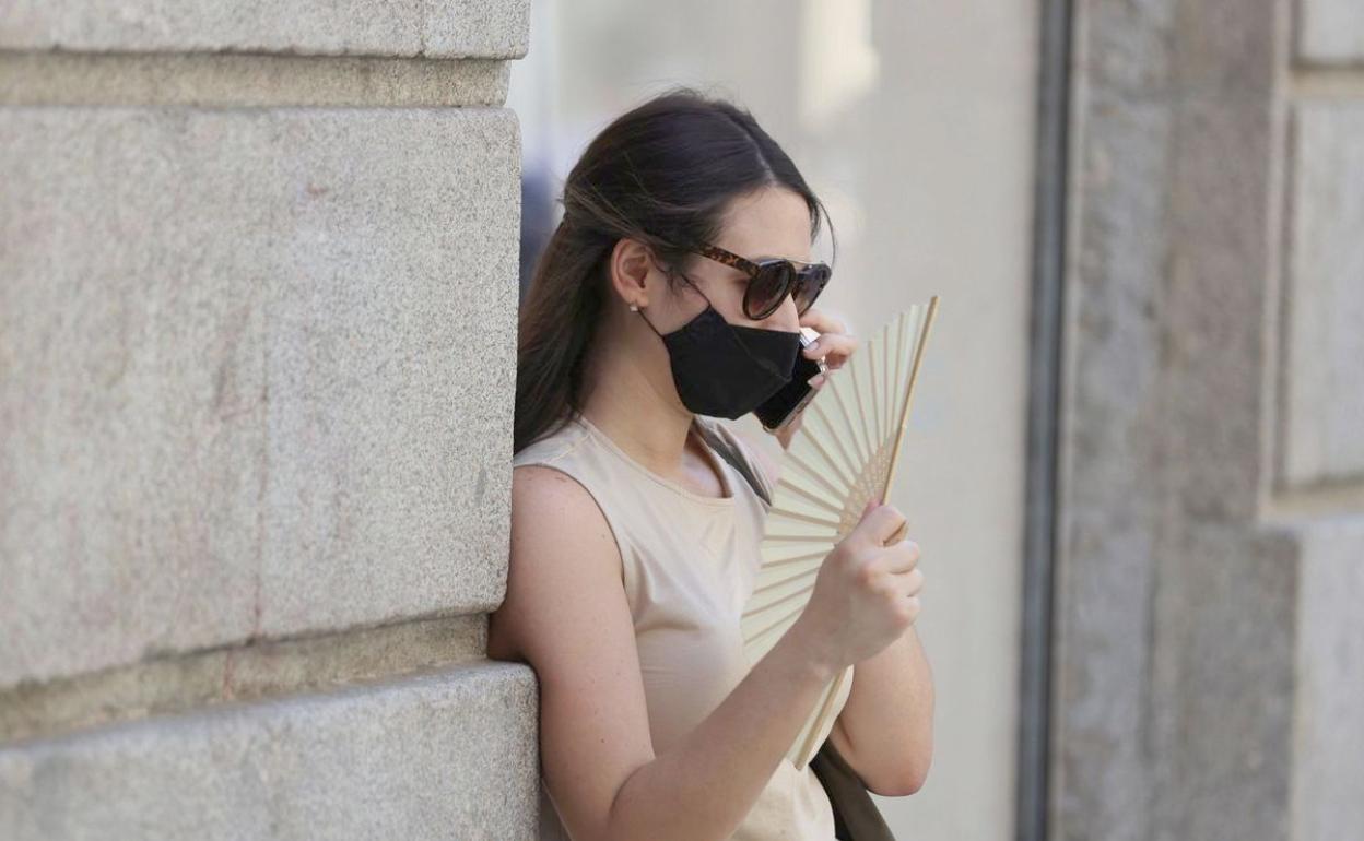 Una mujer alivia el calor veraniego mientras porta una mascarilla. 