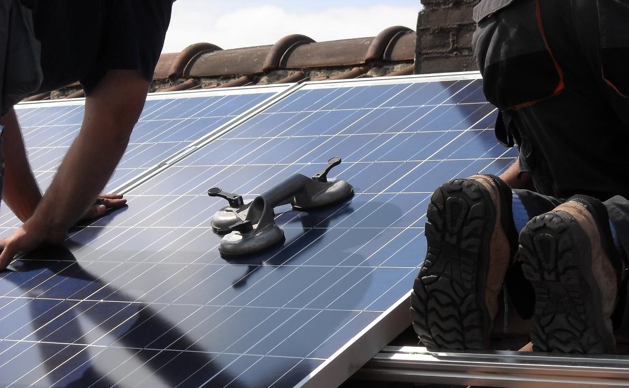 Dos operarios colocan paneles solares en el tejado de una vivienda.