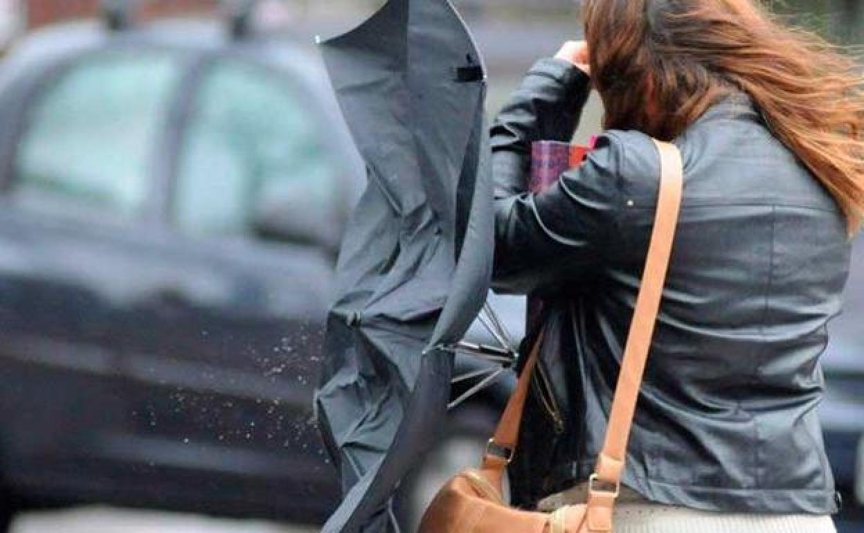 Una mujer sostiene su paraguas ante una fuerte racha de viento. 