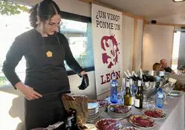 Una cortadora de cecina comparte mesa con diferentes botellas de vino leonés.