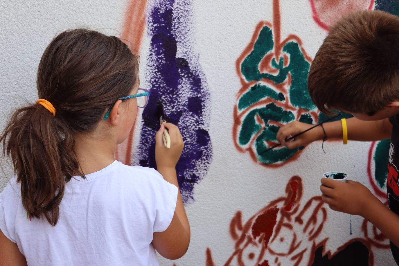 Dos niños pintan uno de los dibujos presentes en el mural.