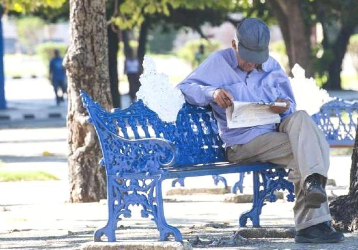 Un pensionista lee el periódico en un banco.