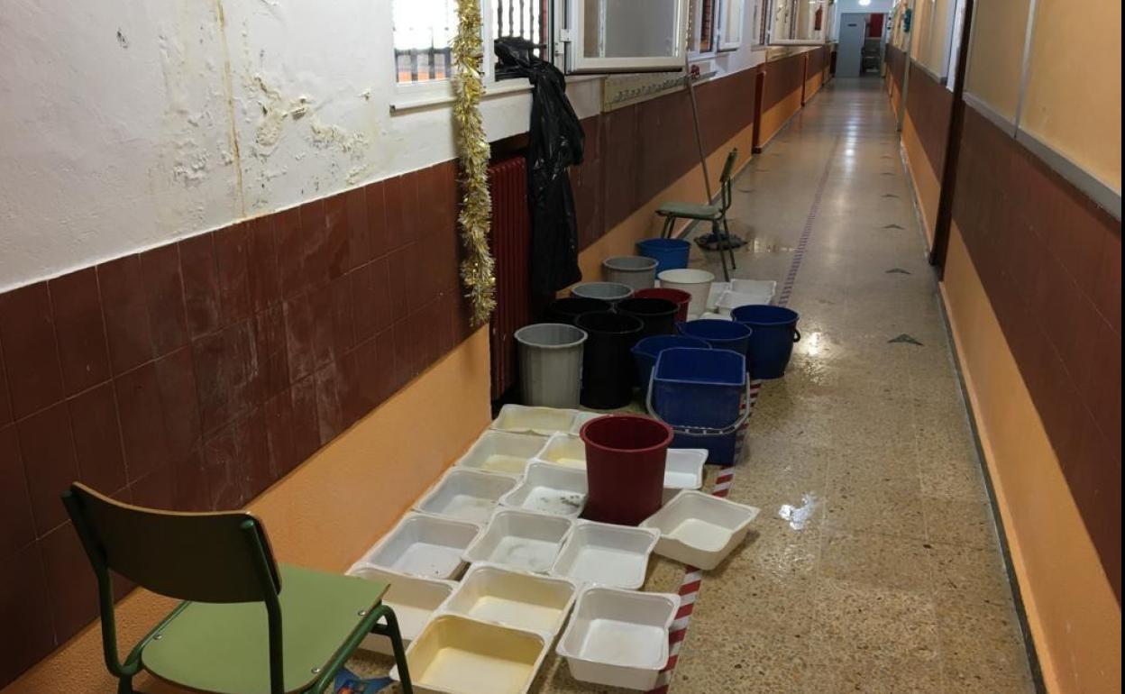 Una pasillo del colegio, lleno de cubos para hacer frente a las goteras.