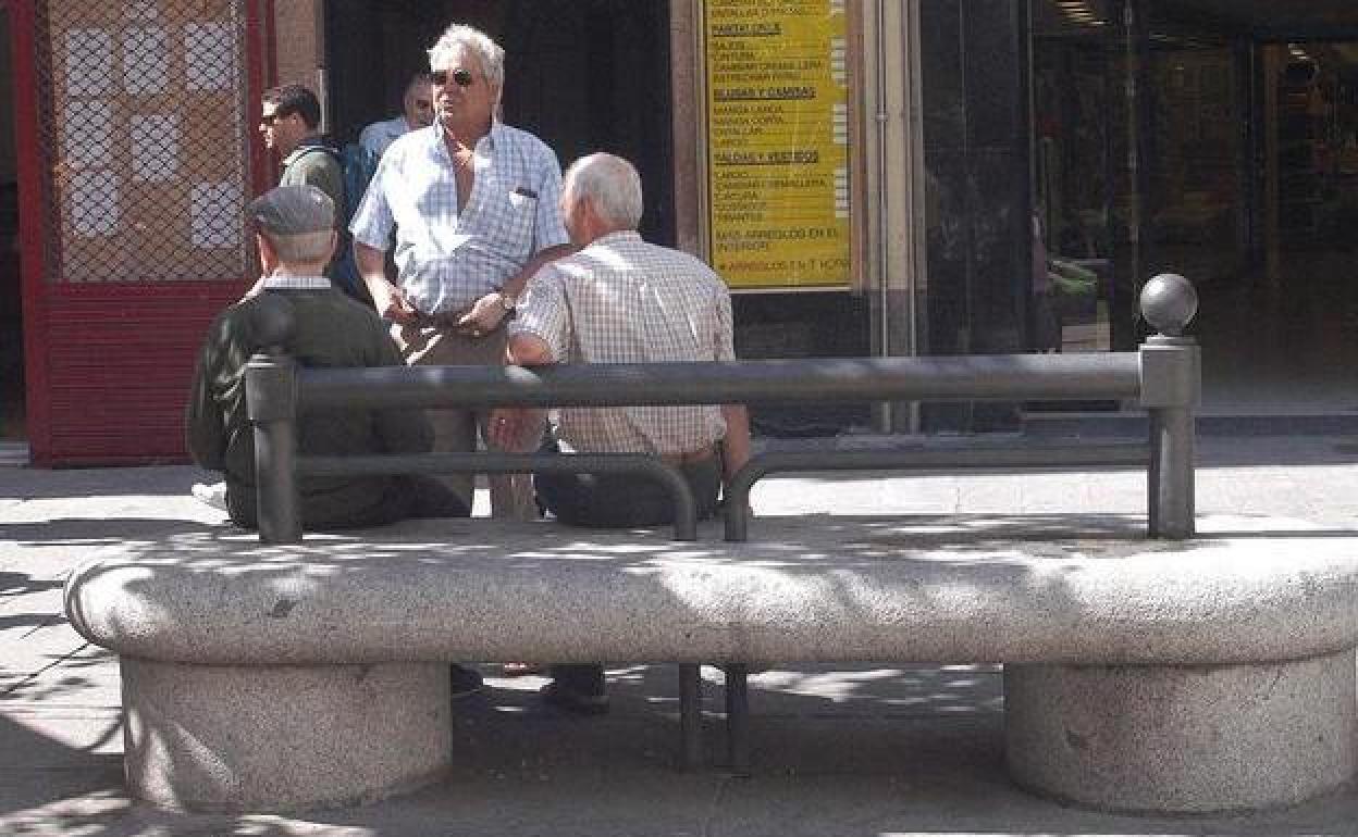 Un grupo de jubilados conversa en un banco.