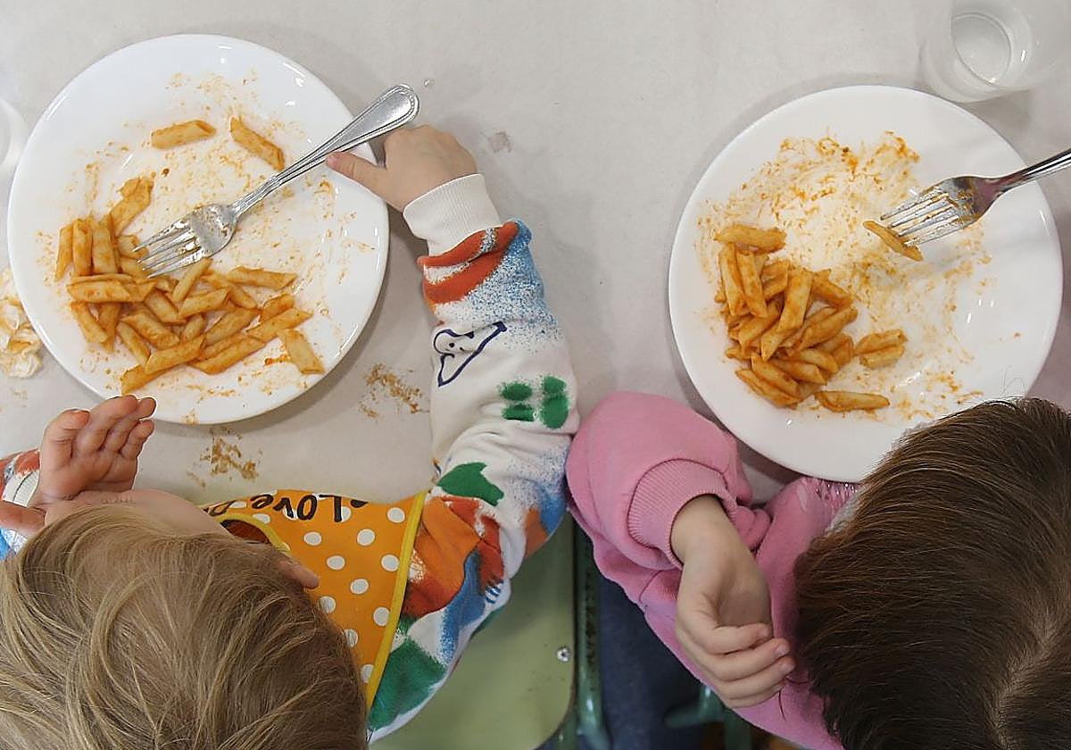 Dos niños comen un plato de macarrones en un comedor escolar.