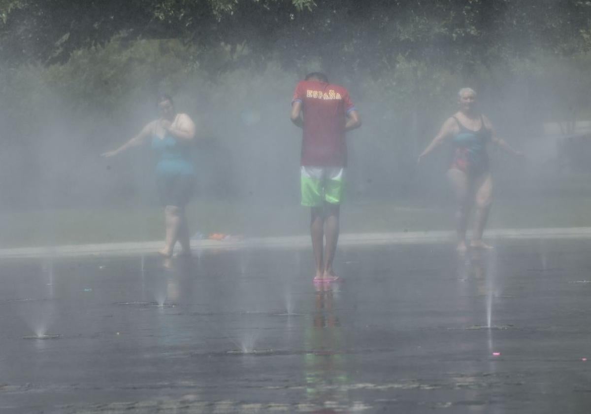 Gente refrescándose en las fuentes de un parque público.