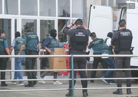 Agentes, algunos encapuchados, depositan en una furgoneta cajas con material incautado en la casa de uno de los detenidos, en Torrelavega.