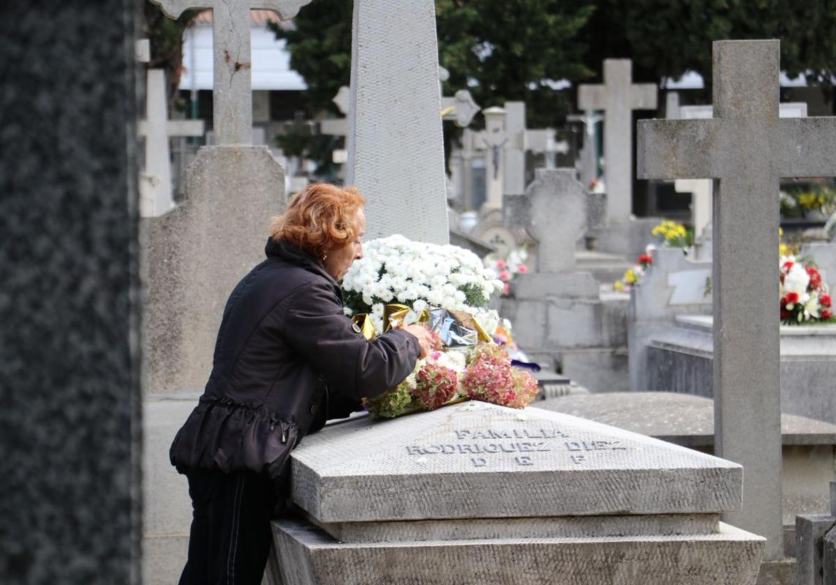 Una mujer coloca flores en una tumba del cementerio de León el día de Todos los Santos.