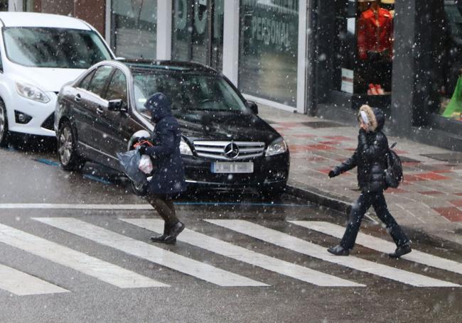 Dos leonesas cruzan un paso de peatones bajo la nieve.