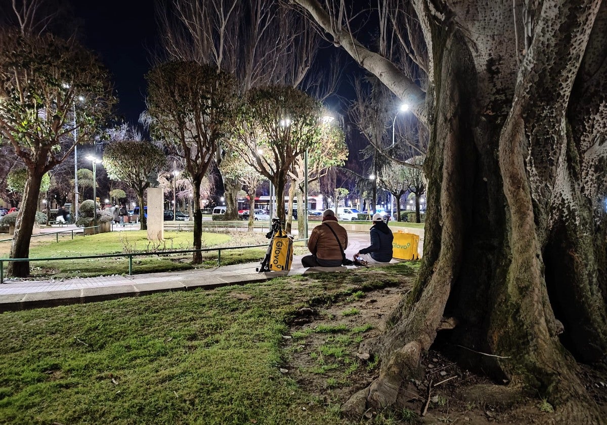 Juan y Miguel conversan en un parque mientras esperan el siguiente pedido.