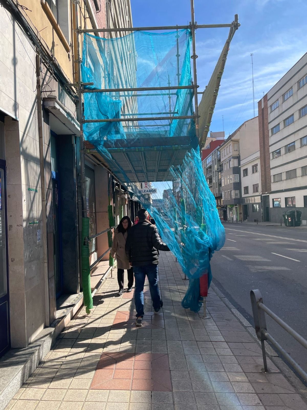 Un vecino aparta la tela que cuelga del andamio para poder pasar por la acera.