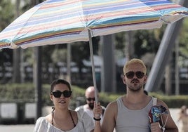 Dos jóvenes se protegen del sol con una sombrilla.