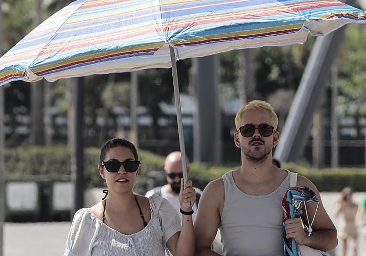 Dos jóvenes se protegen del sol con una sombrilla.