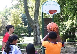 Imagen de unos niños jugando al baloncesto en el Parque Quevedo junto a los voluntarios de la II Edición del Voluntariado Joven de Cáritas de León.