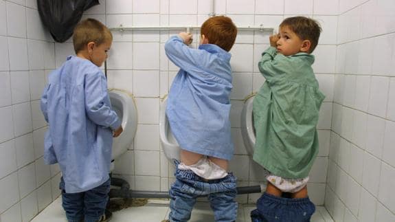 Tres niños haciendo pis en los urinarios del colegio.