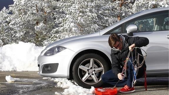 Un hombre pone las cadenas de nieve en su vehículo.