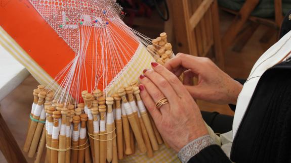 Una señora practicando encaje de bolillos.