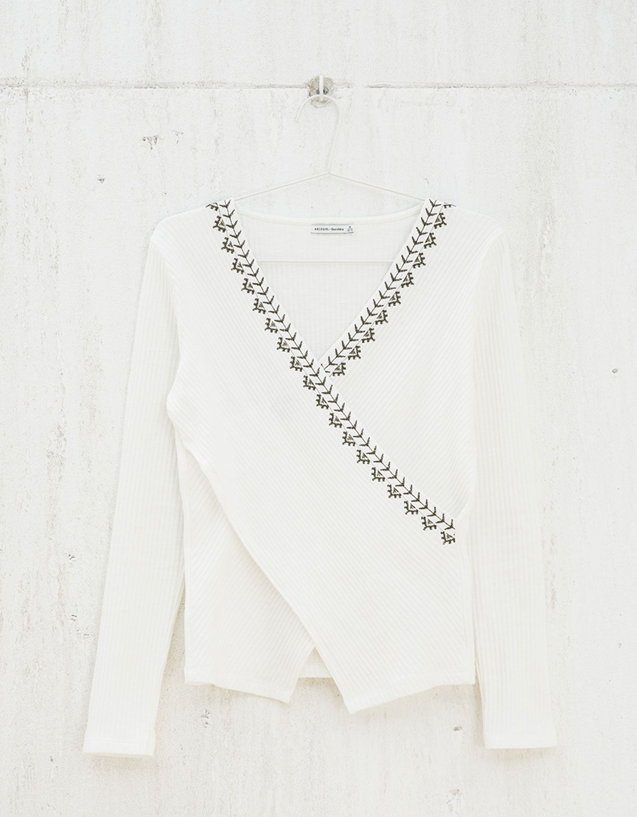 En color blanco, con un pequeño bordado cruzado y escote en pico es este favorecedor top de manga larga (Precio rebajado de 17,99 euros a 10,79 euros).