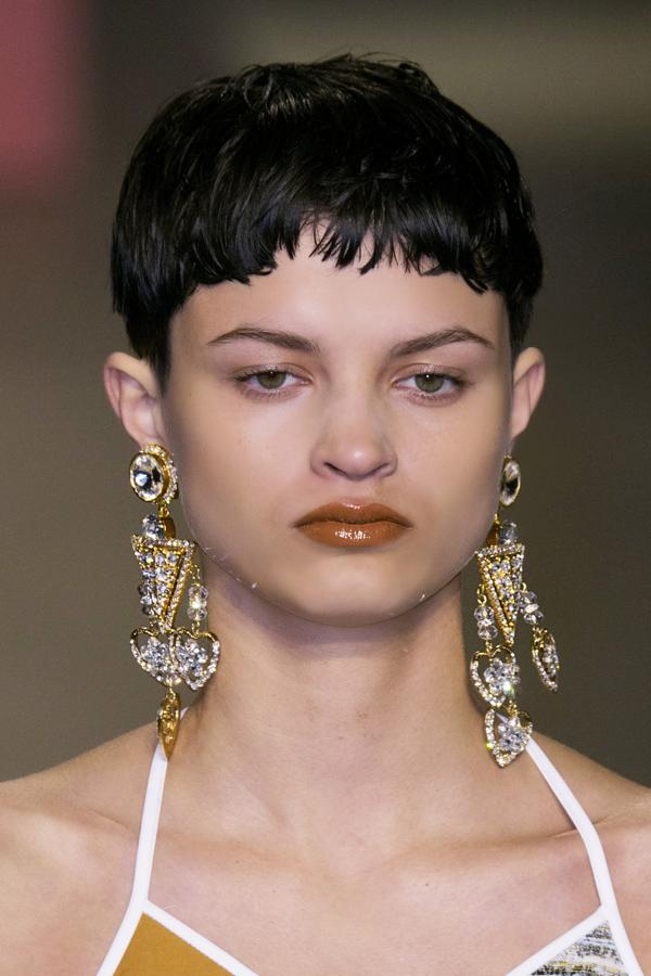 Look: Corte a "tazón" con flequillo corto capeado. Los labios en un marrón con efecto lacado. Plus: Lucir unos pendientes-joya largos.