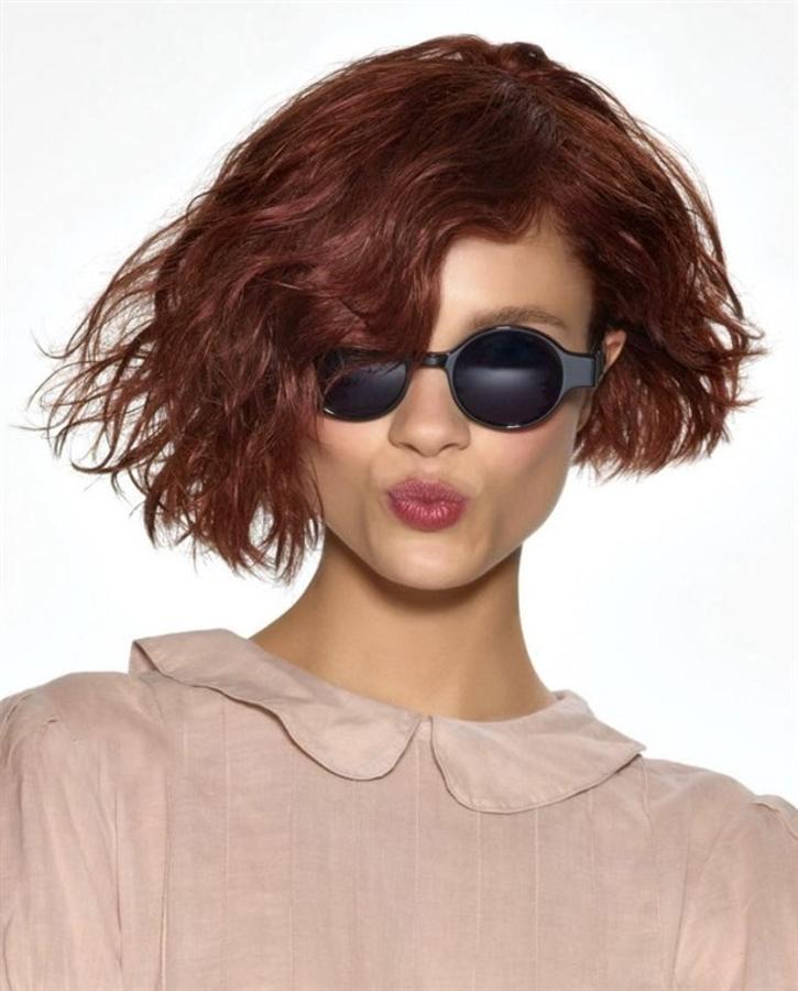 Corte asimétrico de curly bob de ondas naturales en una tonalidad cobriza.