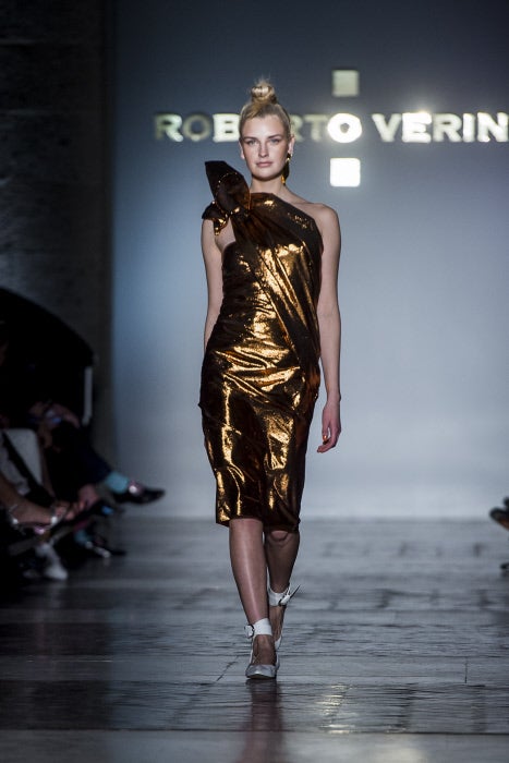 Para la noche, Roberto Verino recurre a los acabados metalizados dando forma a este vestido asimétrico, que el diseñador combina con sanadalias planas en blanco.