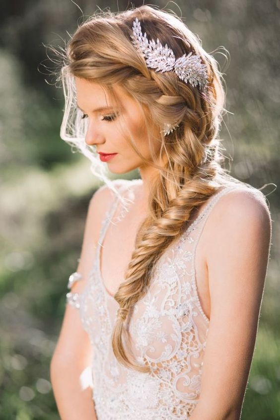Las trenzas siguen marcando la tendencia, y este ejemplo de espiga lateral con mechones sueltos y tocado joya es perfecto para una novia romántica (Foto: Pinterest).