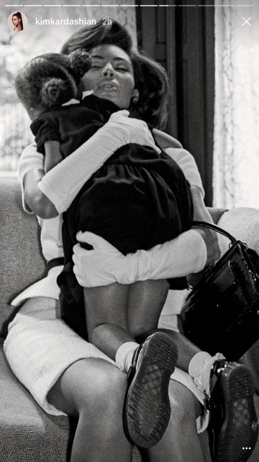 Kim Kardashian con un vestido blanco abrazando a su hija, las dos sentadas en un sofá.