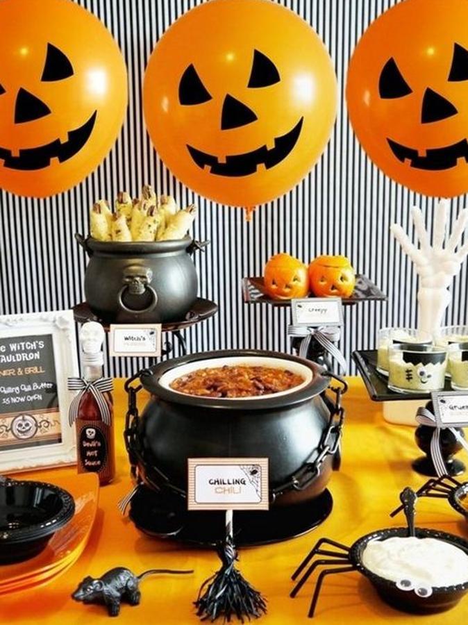 Sin duda, tienes que servir la mesa como en esta imagen. Y es que... ¿qué fiesta de Halloween será si no tienes un buen caldero con tu pócima secreta? Los globos naranjas (y un toque de rotulador negro) te darán mucho juego.