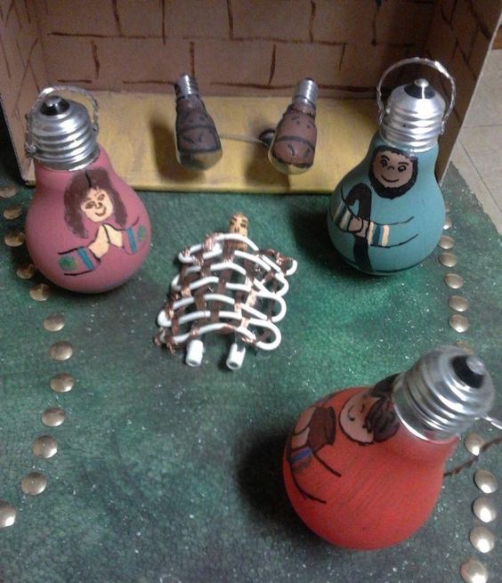 Si alguna bombilla de los adornos ha dejado de lucir del año anterior, ¡tienen utilidad! Puedes aprovechar las divertidas formas de las bombillas para dar vida a tu Belén. Necesitarías bombillas (si es posible de distintas formas y tamaños), colores, y quizás una caja de cartón si quieres crearles un rinconcito a tu Belén. Como ves en la foto, puedes crear la cuna con los cables o utilizarlos para hacer un recinto, unas vayas, ¡e incluso faldas para tus figuras!