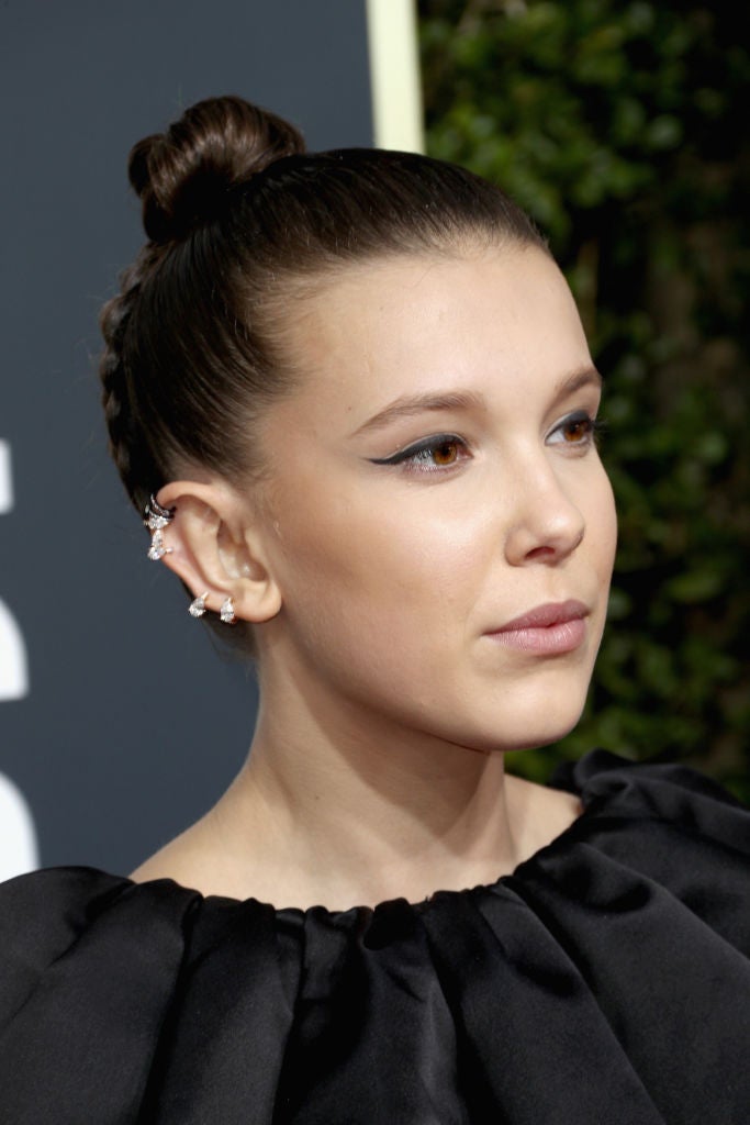 Millie Bobby Brown con moño alto y trenza invertida en la nuca y un discreto maquillaje en el que destacaba su eyeliner negro con rabillo.