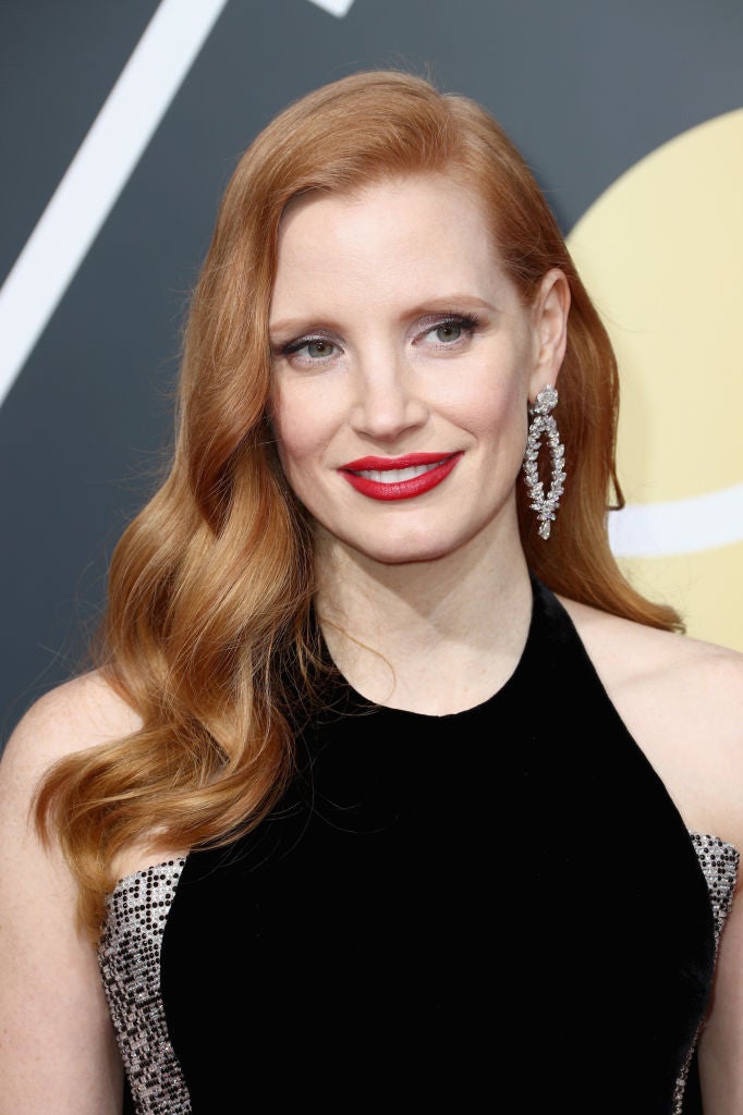Jessica Chastain con un look clásico, melena suelta con ondas y raya lateral, sombras grises metalizadas y labios rojos.