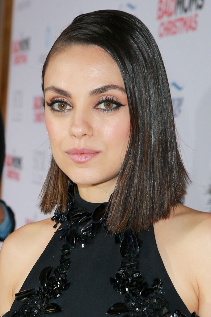 Mila Kunis con melena midi lisa, peinada con raya a un lado y con las raíces muy pulidas.